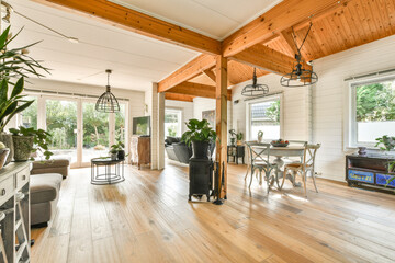 A spacious and inviting modern interior featuring wooden beams, large windows, and a blend of natural light and stylish furniture for a warm atmosphere.