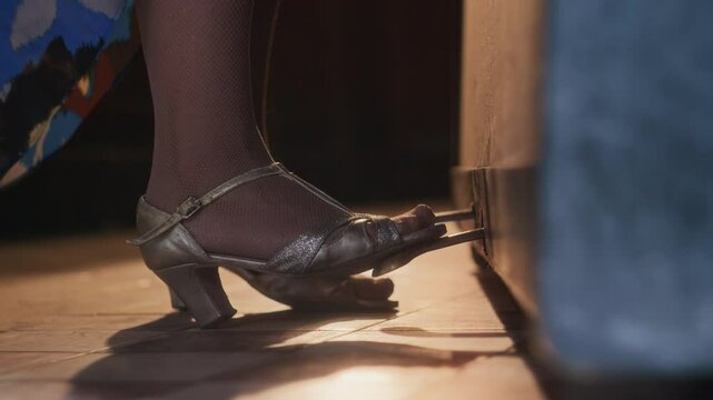 Closeup of unrecognizable female foot in vintage style heel pressing piano pedal during musical performance in warmly lit space