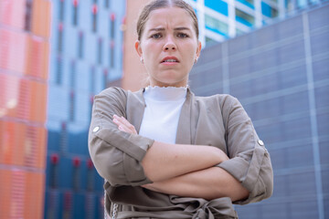Caucasian woman with arms crossed and serious expression standing in front of colorful modern...