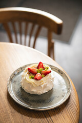 Pavlova cake with whipped mascarpone cream and fresh strawberry slices in cafe.