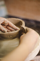 Hands skillfully shape a clay pot in a pottery studio. The workshop encourages creativity and focuses on teaching pottery techniques to beginners in a relaxed atmosphere.