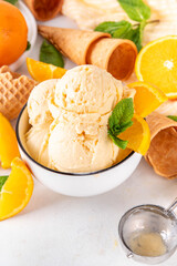 Homemade orange creamsicle ice cream, big bowl with creamsicle gelato, with orange slices and mint, sweet creamy summer dessert, on white kitchen table copy space