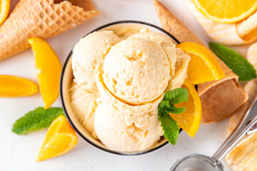 Homemade orange creamsicle ice cream, big bowl with creamsicle gelato, with orange slices and mint, sweet creamy summer dessert, on white kitchen table copy space