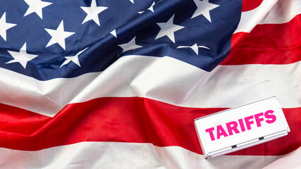 Wood cube tariffs aword on Flag of the United States of America background. USA trade war with word...