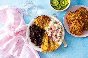 A healthy breakfast featuring brown rice with baked white fish, zucchini-carrot pancakes, Chinese cabbage salad with radish, and a refreshing kiwi dessert for a balanced, nutritious start to the day