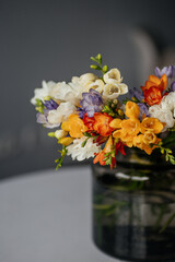 Bouquet of multi-colored freesias in a green glass vase. Spring bouquet of white, yellow, orange and purple freesia. Bridal bouquet. Bright spring flowers