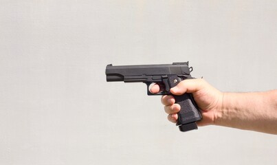 Black gun in a person hand against a light gray background