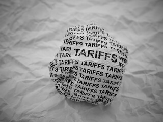 Crumpled paper ball with words Tariffs on a crumpled white paper background.