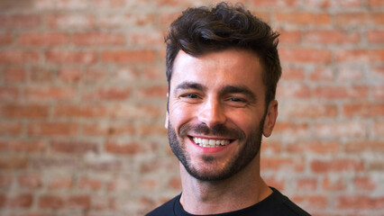 Head And Shoulders Portrait Of Smiling Hispanic Man Standing Against Brick Wall In Coffee Shop