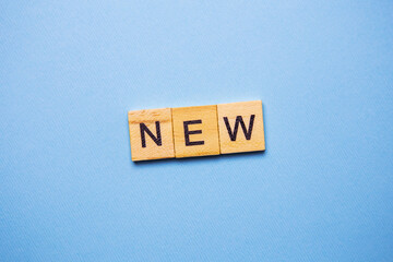 Wooden blocks spelling the word 'NEW' on a light blue background