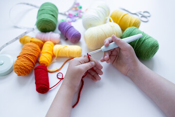 Child crocheting with colorful yarn balls and crochet hook