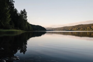 Calm lake with trees reflecting under a soft sky, distant hills backdrop