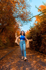 Fototapeta premium Millennial woman walking on an alley covered with autumn leaves