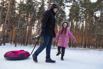 Father and daughter having fun with snow tube in the forest