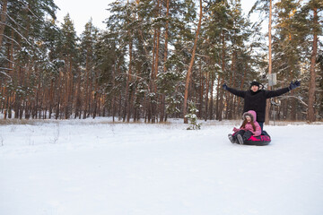 Father and daughter having fun with snow tube in the forest