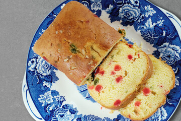 Close-up of a delicious fruit cake served on a blue and white floral plate, on a cement table. Top...