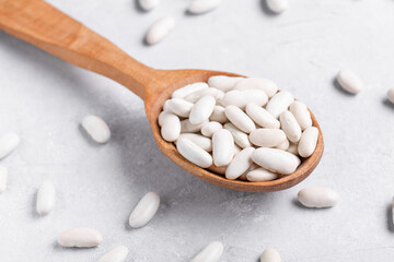 White Navy beans on a wooden spoon on a gray table surface. Popular in Mediterranean diets, these legumes are rich in fiber and protein, often used in soups and stews