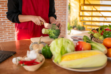 A woman is cutting a broccoli on a wooden cutting board