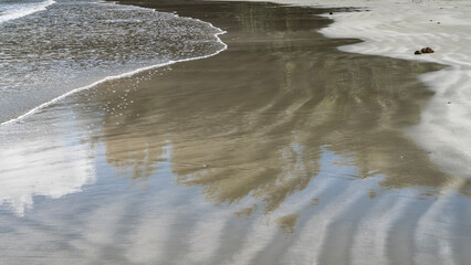 Ocean waves are spreading across the sandy beach. Delicate foam, wavy pattern and reflection on wet smooth sand. Close-up.