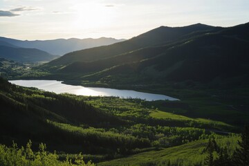 Lake reflects sunlight amid green hills in mountain landscape view