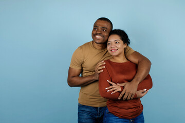 Obraz premium Young black couple embracing affectionately and looking aside at copy space, smiling african american man and woman conveying warmth and emotional closeness, posing on blue studio background
