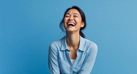 Indonesian 20s woman on blue plain bright background happy laughing hysterical looking at camera portrait banner with copy space ad concept marketing