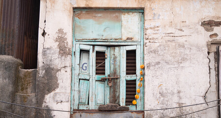 Old house in Mumbai, India, aged rustic facade with broken blue colored window, building with brick and stone