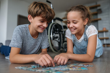 Two children, a boy and a girl, are happily assembling a jigsaw puzzle on the floor. The boy is around 12 years old, and the girl is about 10 years old. A wheelchair is visible in the background.