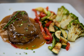 Delicious steak cooked rare, smothered in a tasty gravy and paired with grilled vegetables such as broccoli, bell peppers and zucchini, satisfying part of a healthy diet when consumed in moderation
