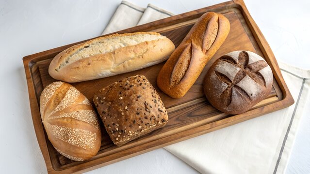 An assortment of freshly baked bread rolls and a baguette are arranged on a rectangular wooden tray.