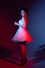 Elegant woman in a sparkling white dress with heels poses against a colorful background