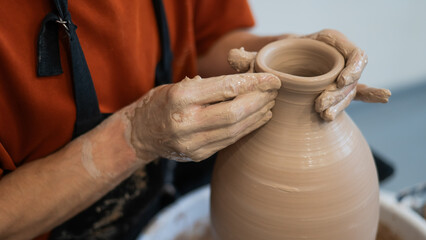 Close-up of a potter's hands making a ceramic vase on a potter's wheel. 