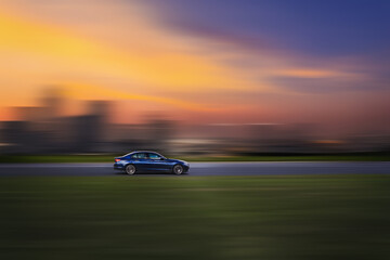 Side view of a fast-moving car, with a blurred sunset sky in the background. Car on a motion blurred background