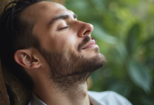 Young man with closed eyes. Man resting in forest reduces fatigue and breath fresh air, visualizing and meditating outdoors. No stress concept. Close up