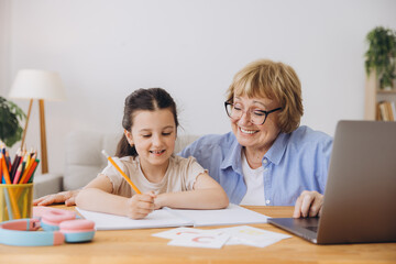 Happy grandma helping adorable preschool granddaughter school kid with homework task. Positive...