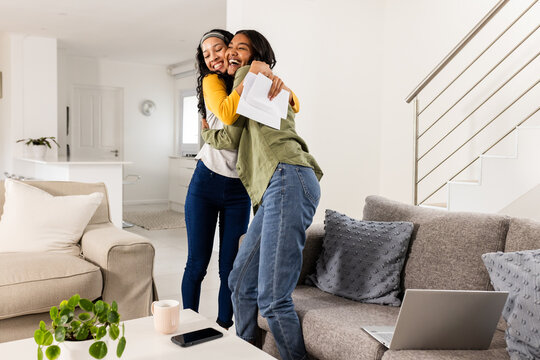 Young girl friends hugging joyfully at home, celebrating good news