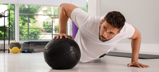 Obraz premium Athletic man doing push ups with medicine ball in modern gym