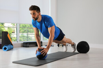 Athletic man doing plank exercise with medicine ball in modern gym