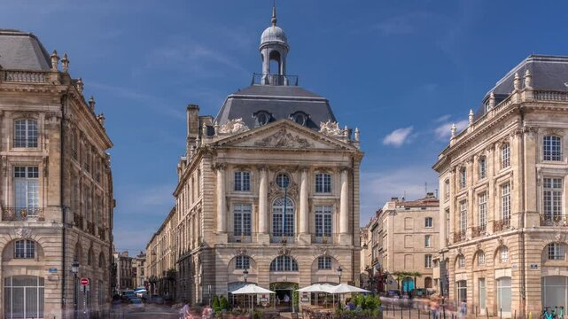Place de la Bourse timelapse hyperlapse in Bordeaux, France, with restaurants surrounded by classic architecture under a cloudy blue sky. People walking around the main square and central streets