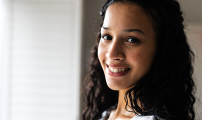 At home, Smiling woman with curly hair looking at camera, exuding warmth and confidence, copy space