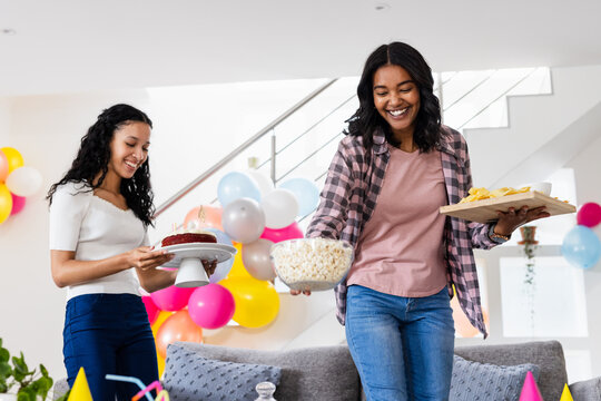 Smiling diverse female friends preparing snacks and cake for birthday party at home