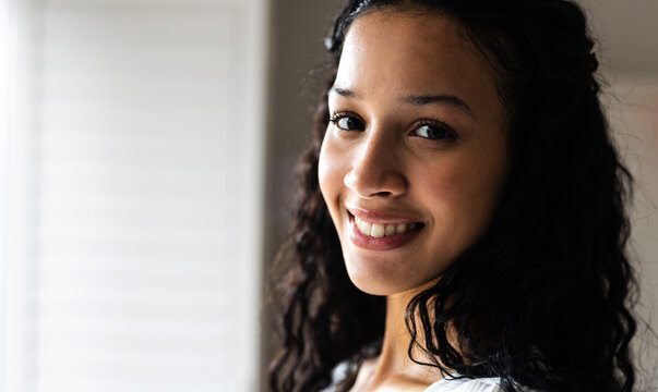 At home, Smiling woman with curly hair looking at camera, exuding warmth and confidence, copy space