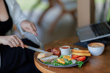 A young woman works while having breakfast at an outdoor café, reflecting the modern flexible lifestyle.