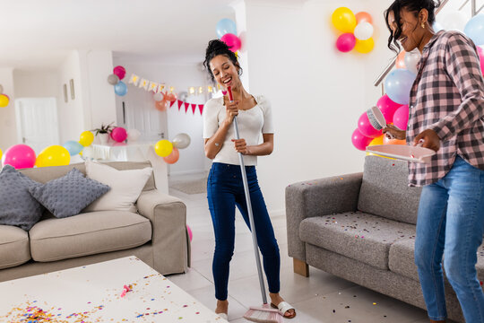 Celebrating at home, diverse female friends cleaning up after party with balloons and confetti