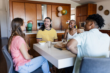 Diverse friends enjoying conversation and laughter around dining table at home gathering