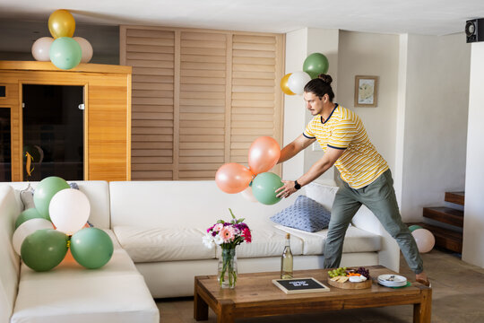 Man decorating living room with colorful balloons for party celebration, at home - Powered by Adobe