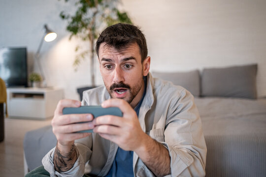 Surprised man playing mobile game at home in living room