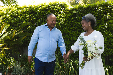 At wedding, Senior couple holding hands and smiling in garden with bouquet of flowers