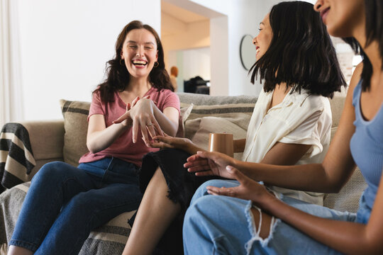 Diverse female friends laughing and chatting on couch, enjoying quality time together at home