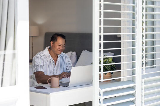 Senior man using laptop at home, smiling and enjoying morning coffee